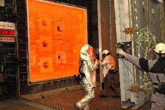 Workers in protective suits stand near an open, intensely glowing industrial furnace during a test or operation.