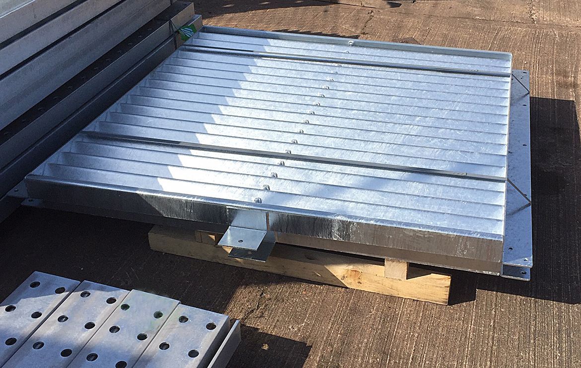 A stack of perforated, galvanized steel metal planks or floor grating panels on a wooden pallet outdoors.