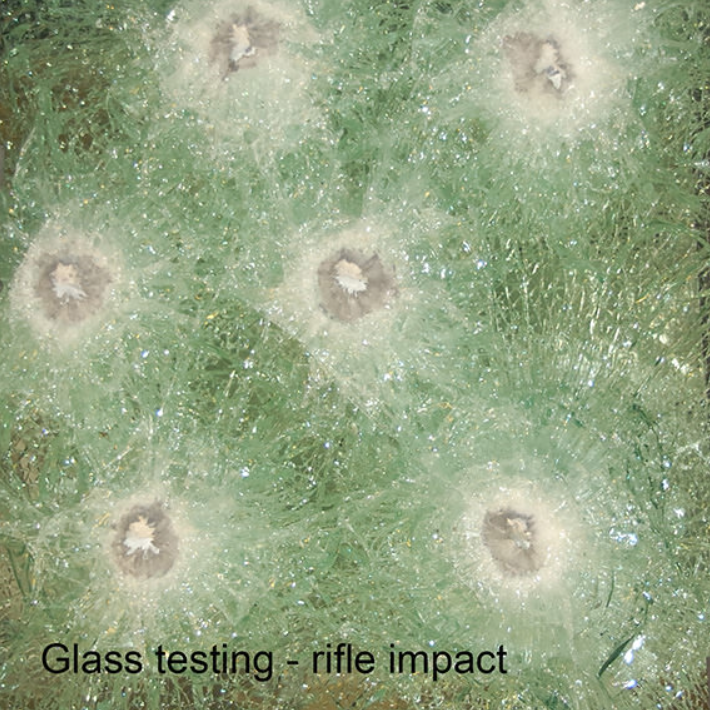 Bullet-shattered green glass showing circular impact patterns from rifle fire testing.