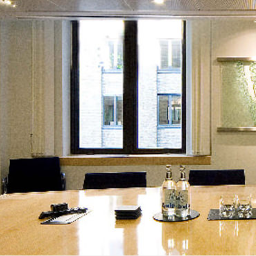A conference table with glasses of water, pens, and notepads in a room with a large window overlooking a building.