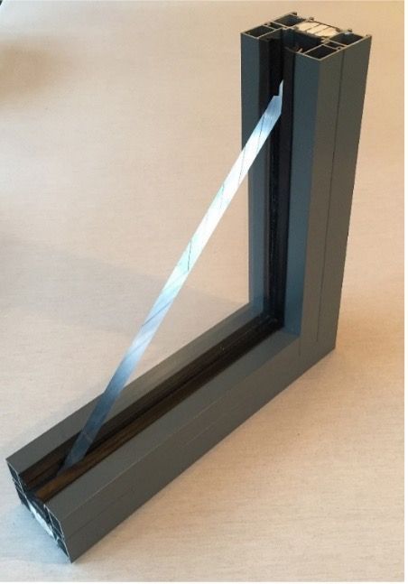 A corner section sample of a dark grey aluminum window frame with a single pane of glass held by black rubber gaskets.