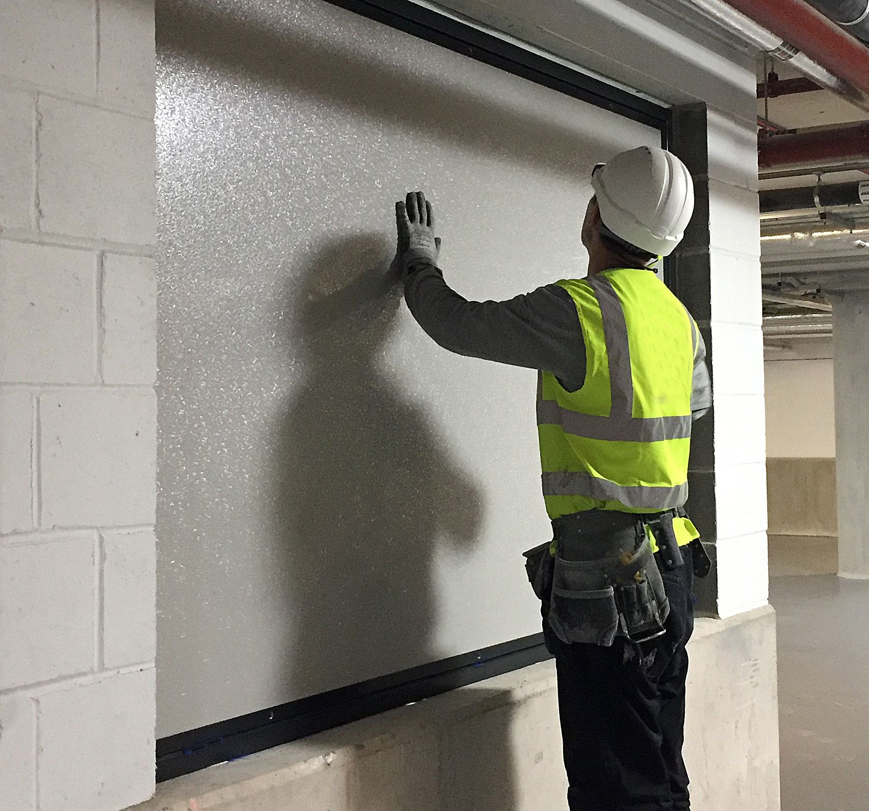 A worker in a high-visibility vest and hard hat touches the textured surface of a large, frame-mounted panel.
