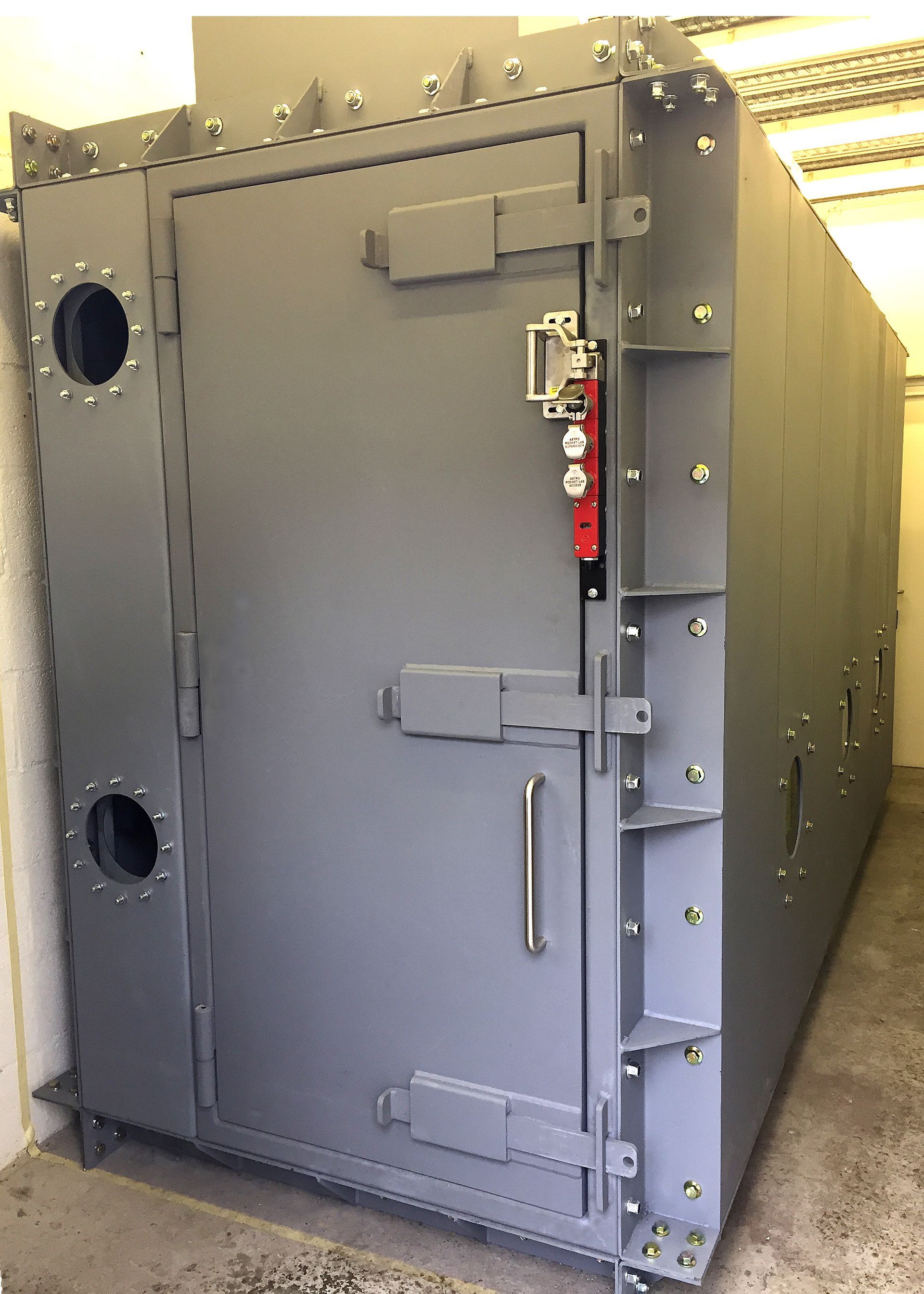 A large, grey, heavy-duty industrial pressure vessel or vault with a reinforced locking door and circular ports.