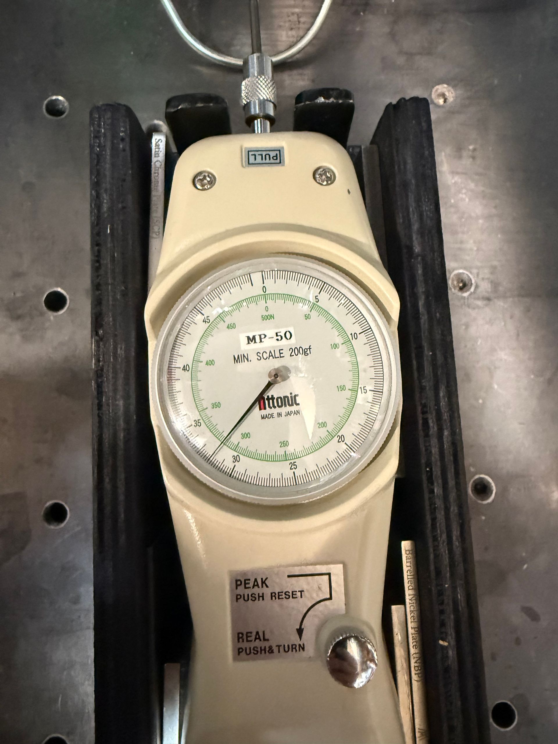A beige Chatillon force gauge sits in a metal cradle, showing a measurement on its circular analog dial.