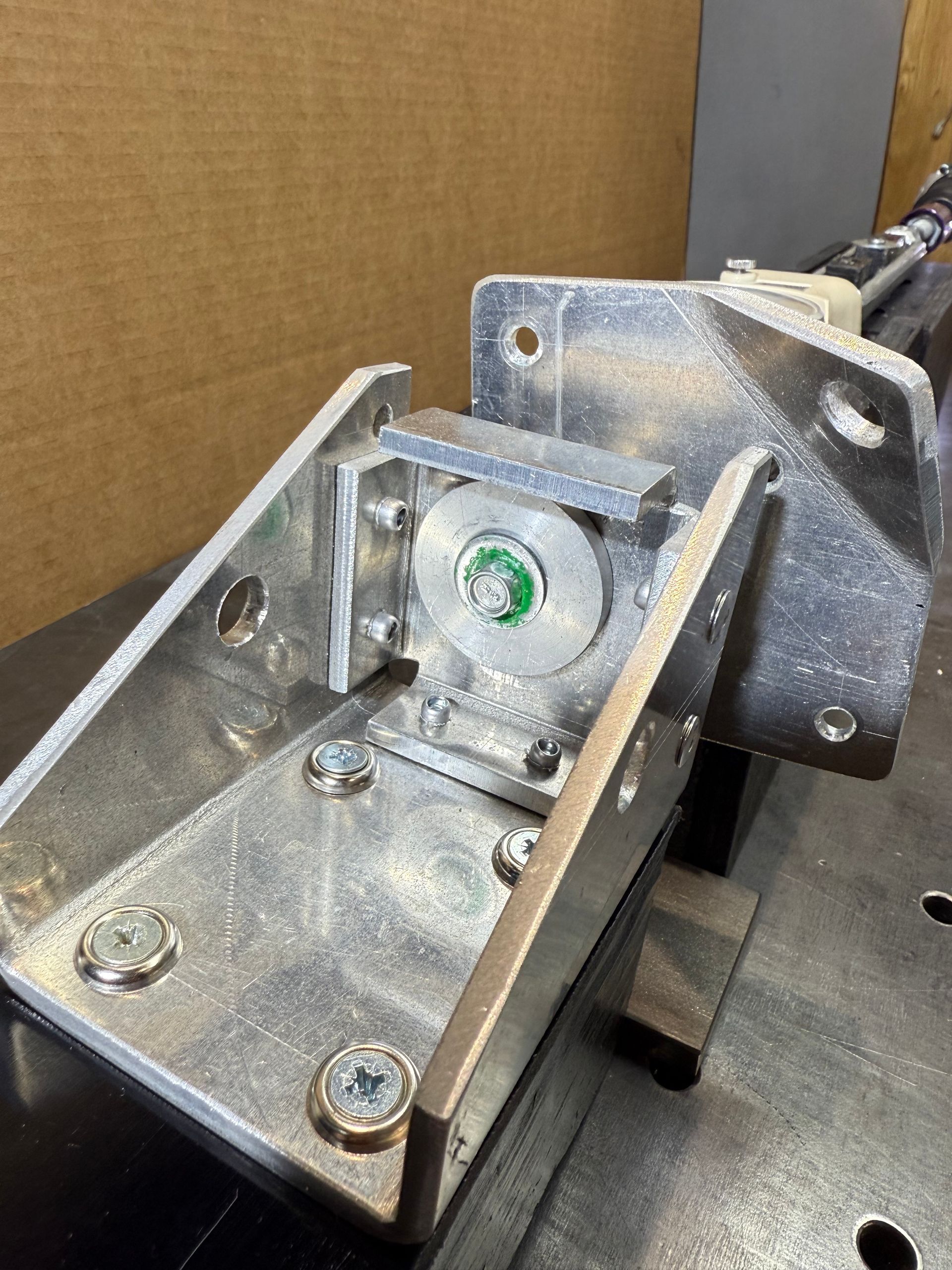 A close-up shot of a silver, custom-machined metal bracket mounted to a surface, featuring a central circular joint component.