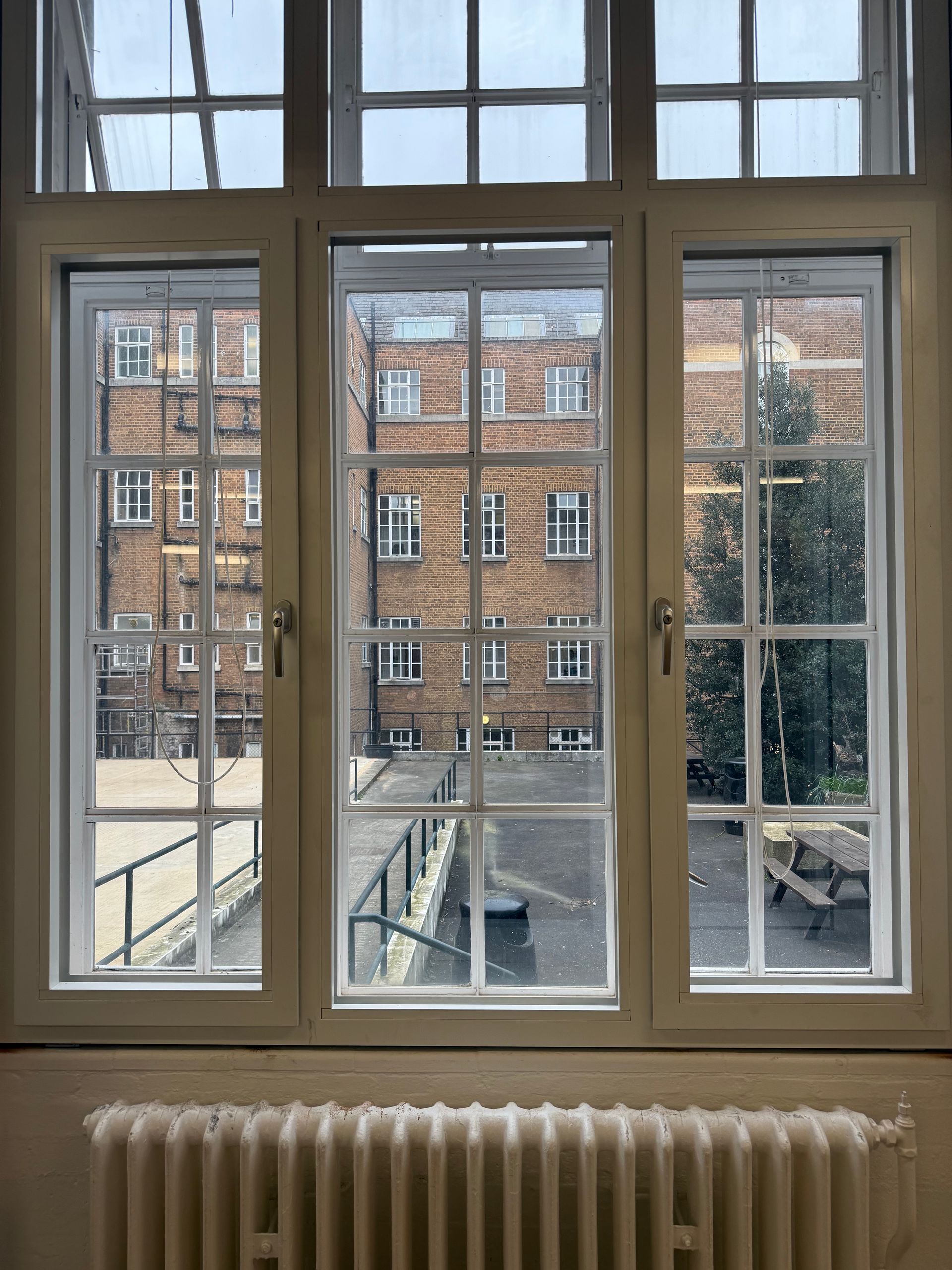 A view through a white-framed window looking out at a brick building courtyard with a radiator below.