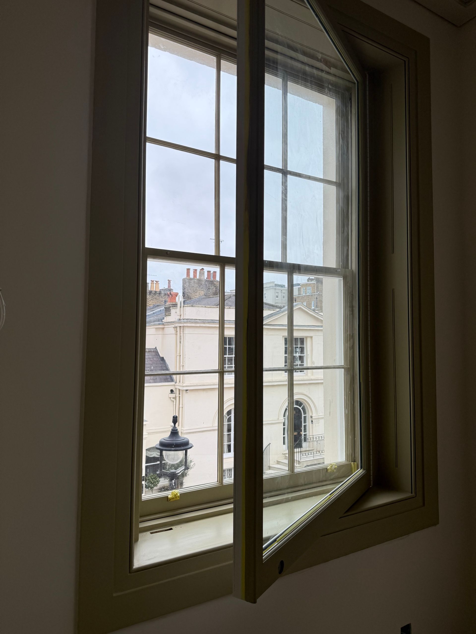 A multi-pane window is partially open, looking out onto a street with beige buildings and an ornate lamp post.