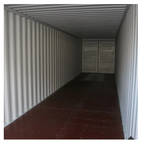 Inside a long, empty shipping container with corrugated white walls and a dark, flat floor, looking toward closed doors.