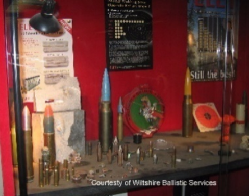 Display case at Wiltshire Ballistic Services featuring various ammunition, artillery shells, and a bullseye target.