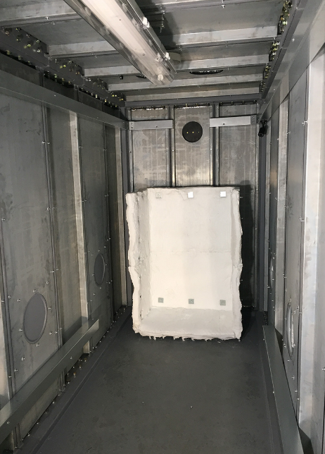 A white rectangular foam block stands inside a long, narrow industrial corridor made of gray metal panels.