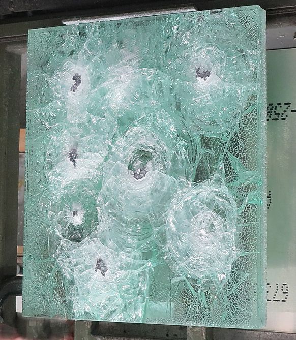 A thick, light-green pane of bulletproof glass with seven distinct impact marks and radial spiderweb fracturing.