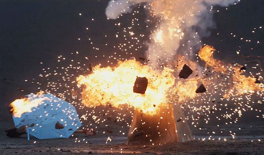 A bright orange fireball explodes in a dark space, scattering debris near a fallen white umbrella.