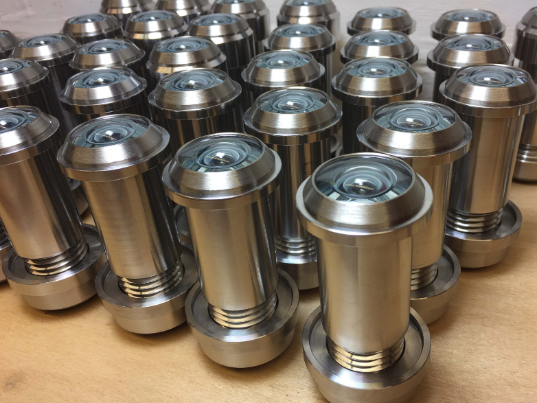 A group of silver-colored metal door peepholes with glass lenses, standing upright on a wooden surface.