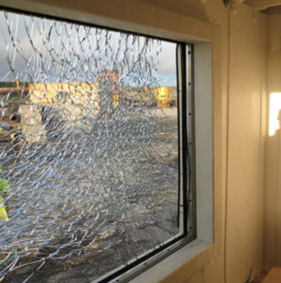 A shattered rectangular window pane with a web-like crack pattern, looking out toward an industrial construction site.