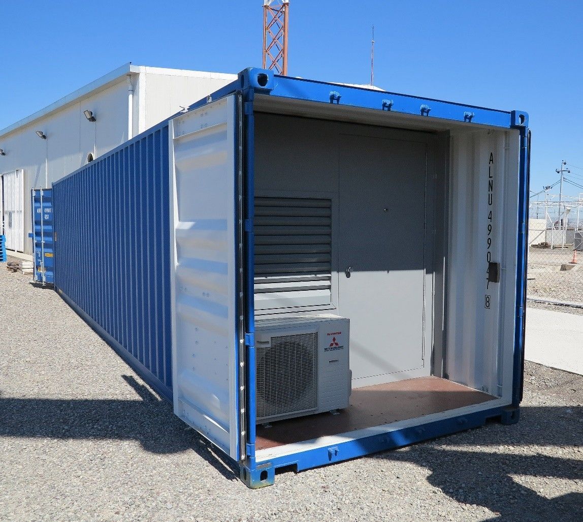 A blue shipping container on a gravel lot holds an air conditioning unit and a gray access door.