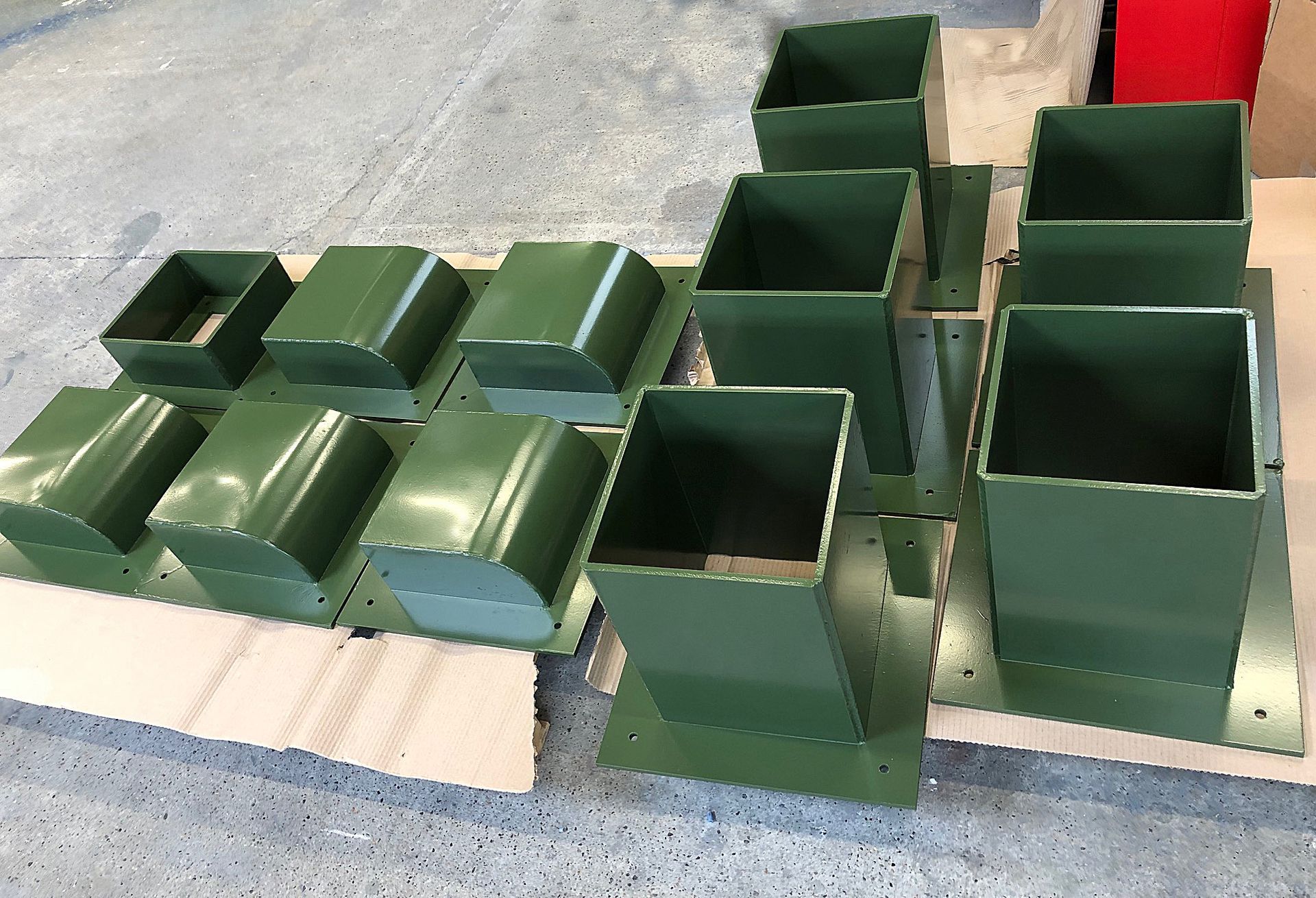 A collection of green, box-shaped metal vents or bases arranged on a light surface in a workshop.