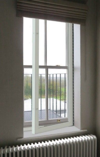 A white-framed window slightly ajar, revealing a view of a metal balcony railing and greenery, with a radiator below.