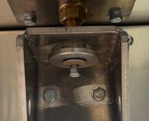 Close-up of a metal U-shaped bracket mounted to a flat surface with hex bolts, washers, and a brass threaded fitting.