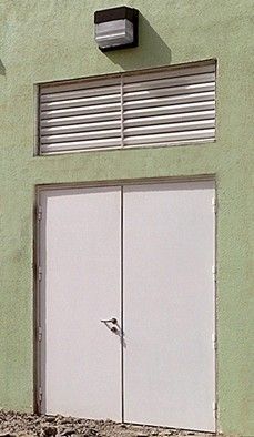 Double white doors on a green wall, featuring a vent above the doors and a light fixture mounted at the top center.