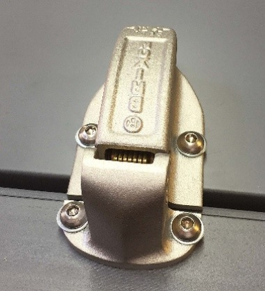 A silver, spring-loaded metal latch mounted with four screws on a gray surface. The word