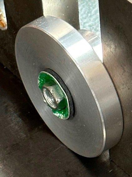 A metal circular wheel mounted with a nut on a bolt, positioned between two vertical metal plates.