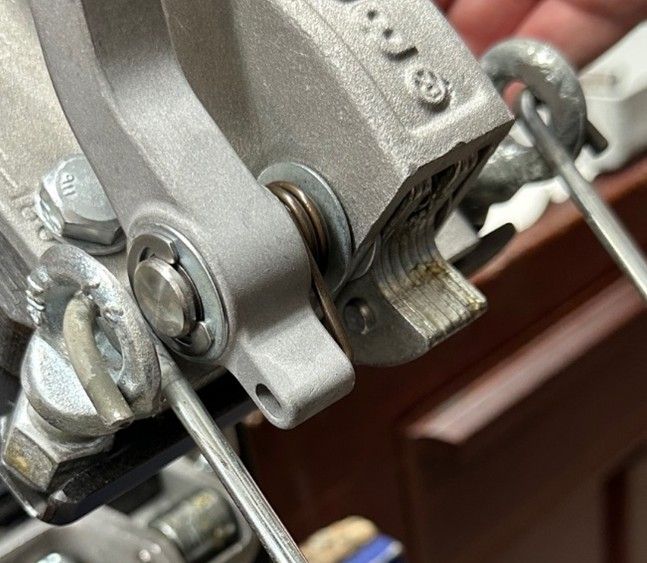 Close-up of a metal mechanical clamp mechanism with a wire inserted, secured by a pin and spring-loaded hinge.