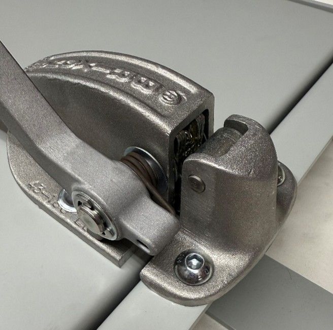 A heavy-duty, industrial-style gray metal latch mechanism mounted on a gray surface, shown in a closed, locked position.