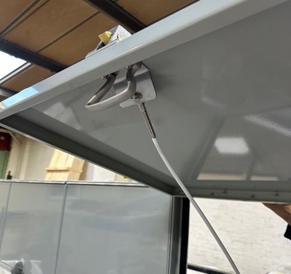 Close-up of a metal cabinet lid held open by a thin white tether cord attached to a bracket on the underside.