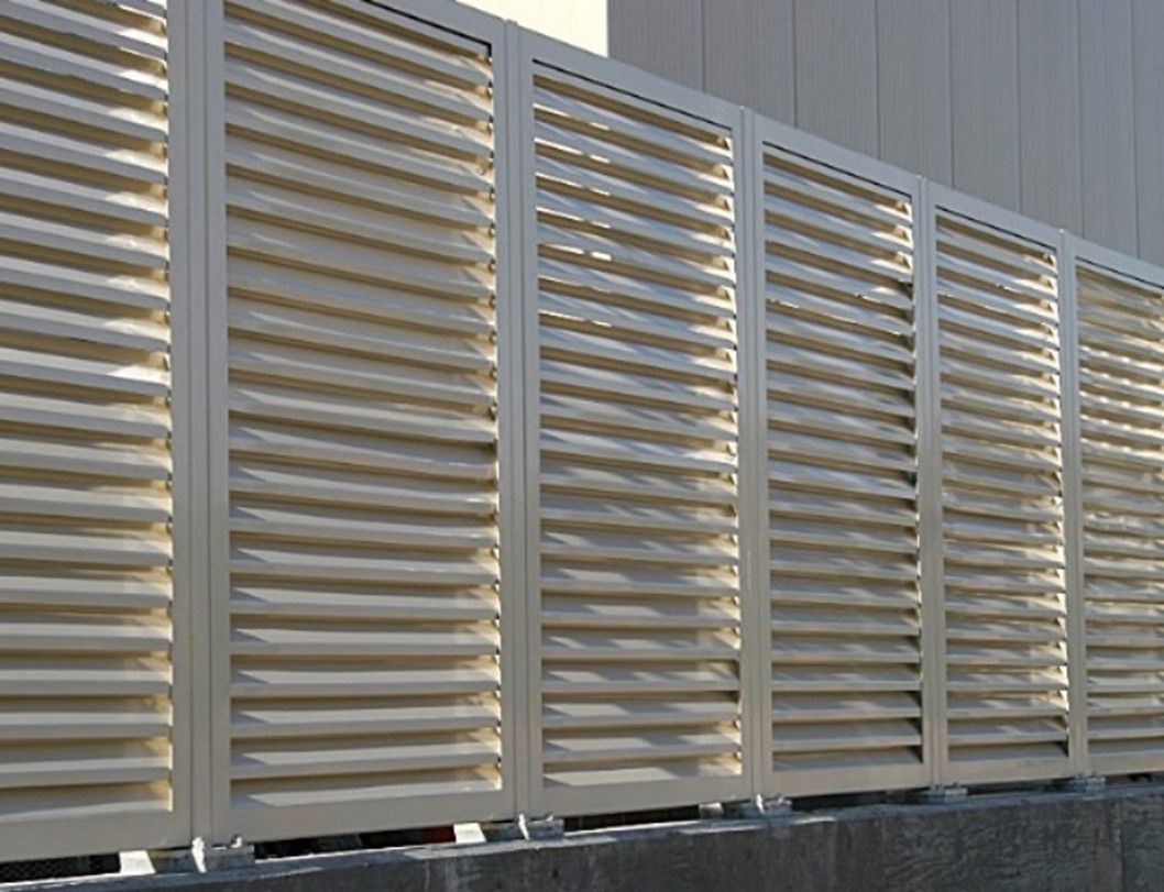A row of cream-colored metal louvered panels installed as an outdoor privacy screen atop a low stone wall.