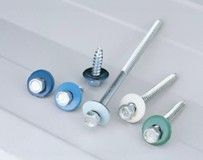 Several metal roofing screws with colored rubber washers, arranged on a light grey, corrugated metal surface.