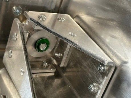Close-up of a metal mechanical assembly with a green-centered circular component housed inside a structural bracket.