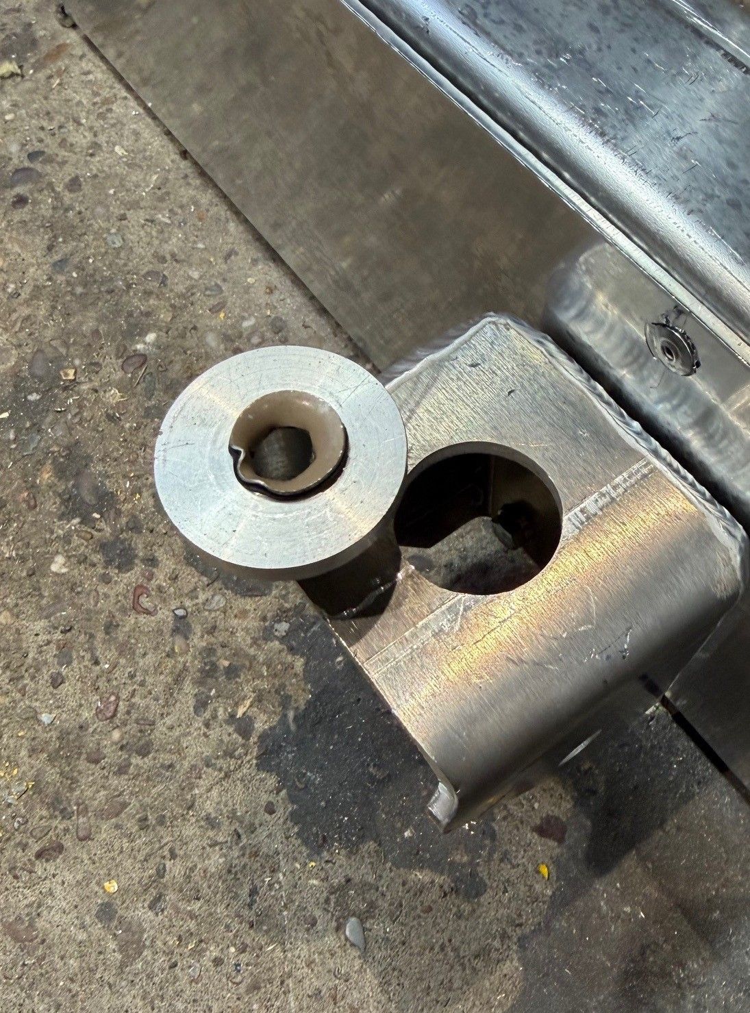 A close-up view of a metal hinge assembly showing a detached, circular bushing next to a corresponding hole in the bracket.