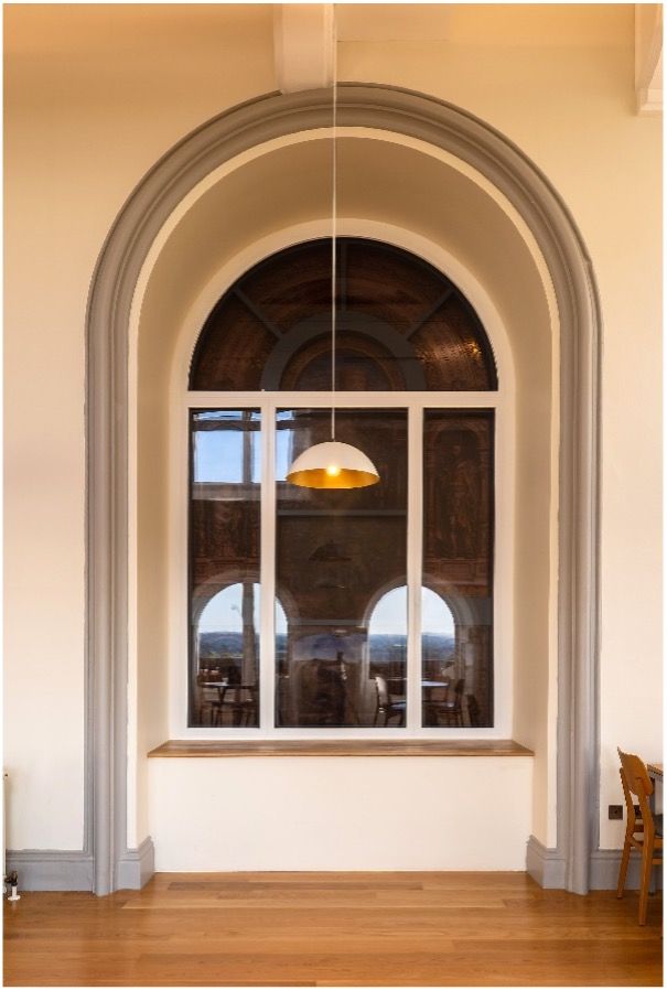 A tall, arched window with white trim and a gold-lined pendant light hanging in front of a wooden floor.