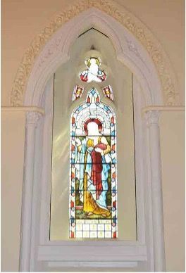 Stained glass window set in a stone arch featuring a figure in flowing robes, with a decorative trefoil detail above.