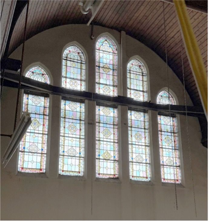 Five arched stained-glass windows with a geometric grid pattern set into a curved, wood-paneled ceiling inside a building.