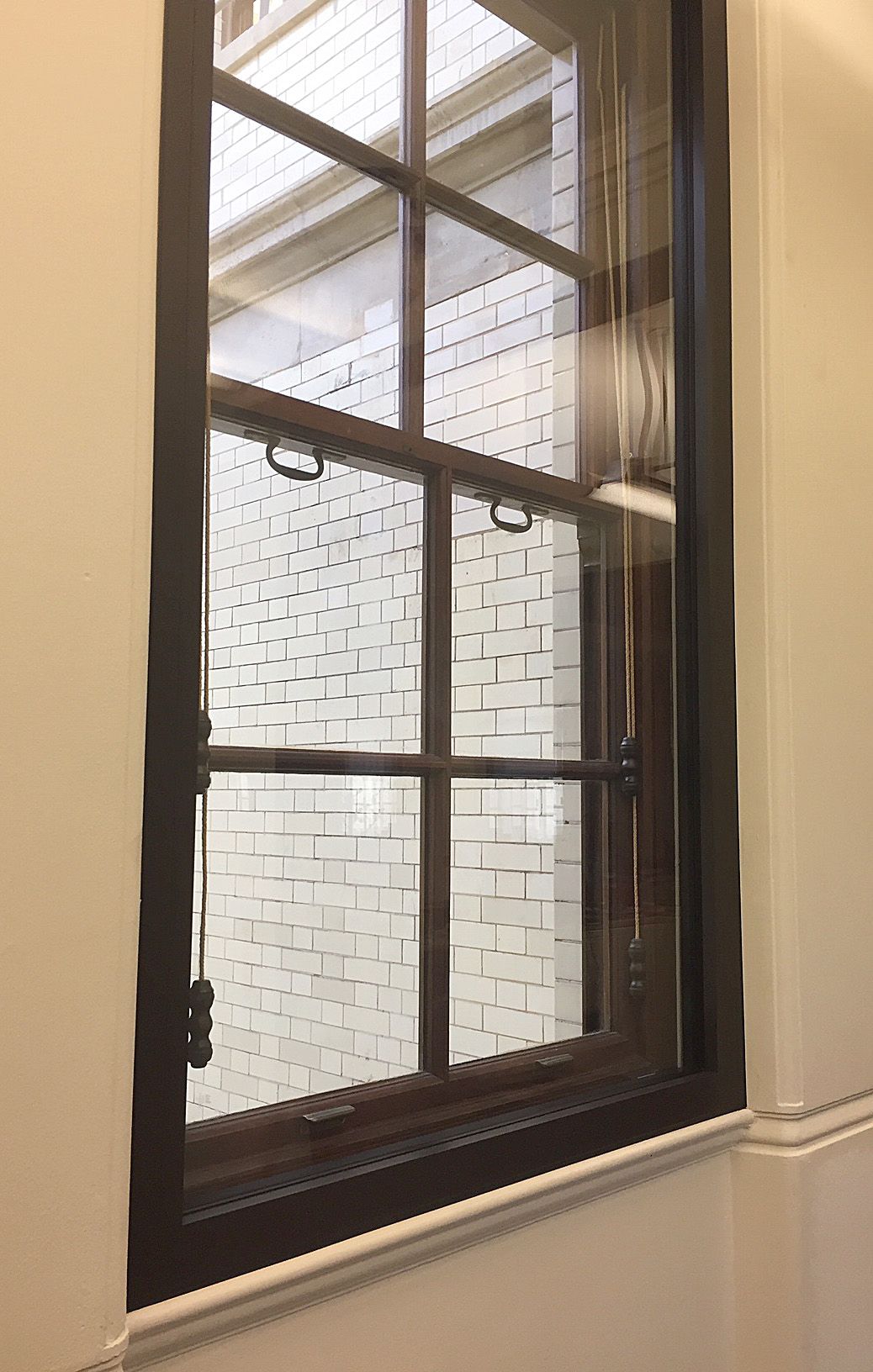 A dark-framed window with a vertical grid looking out onto a white brick wall.