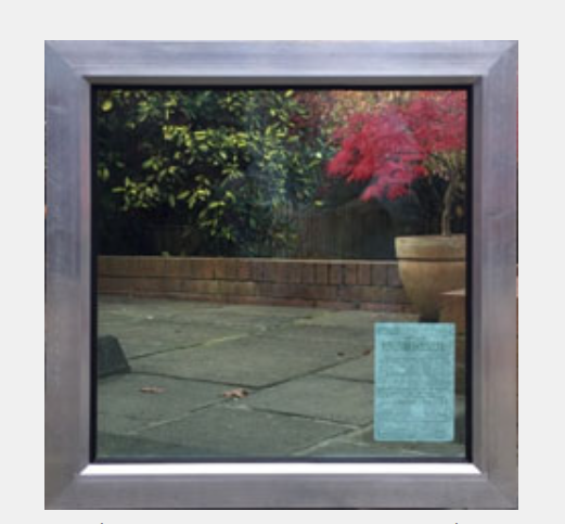 A square window with a metallic frame reflecting a patio, green bushes, a red tree, and a planter.