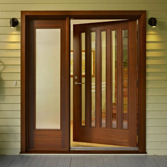 A wooden front door with vertical glass panels and a matching side light, illuminated by two wall sconces on pale siding.