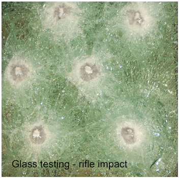 A close-up view of bulletproof glass with six distinct impact points from rifle fire, showing spiderweb cracking.