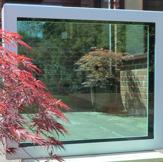 A bright white window frame reflecting a patio, brick wall, and lush green tree, with a red-leafed bush in the foreground.