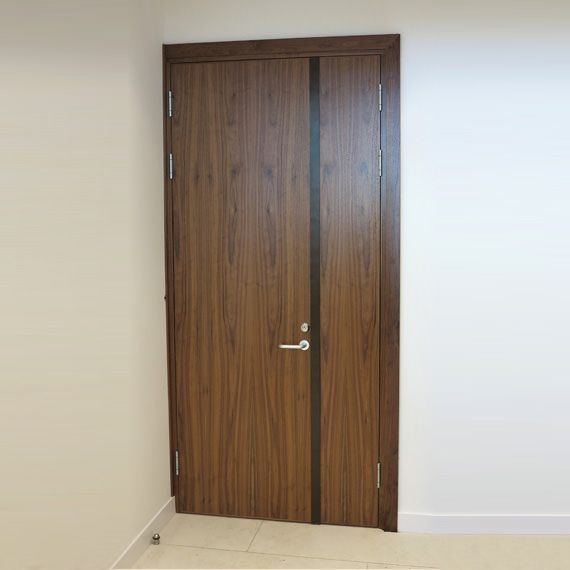 A dark wood door with a vertical black accent stripe and a silver handle, set in a plain, light-colored interior wall.