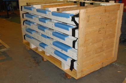 A wooden shipping crate containing several stacked rectangular panels protected by blue foam edge guards.