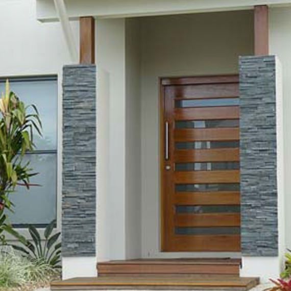 A wooden front door with horizontal glass panels, flanked by two gray stone pillars under a covered entryway.