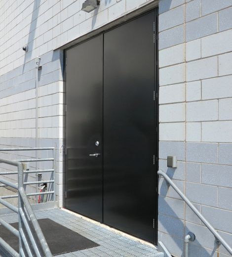 Black double doors on a grey concrete block wall next to metal handrails and a ramp.