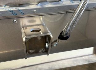 A metal bracket mounted to a silver panel, with a thick steel wire cable attached to the side by a bolt.