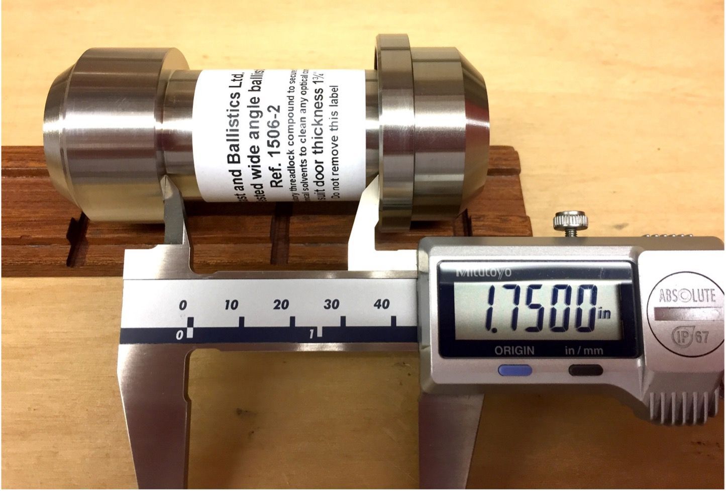 Digital calipers measuring the length of a cylindrical, stainless steel component on a wooden surface.