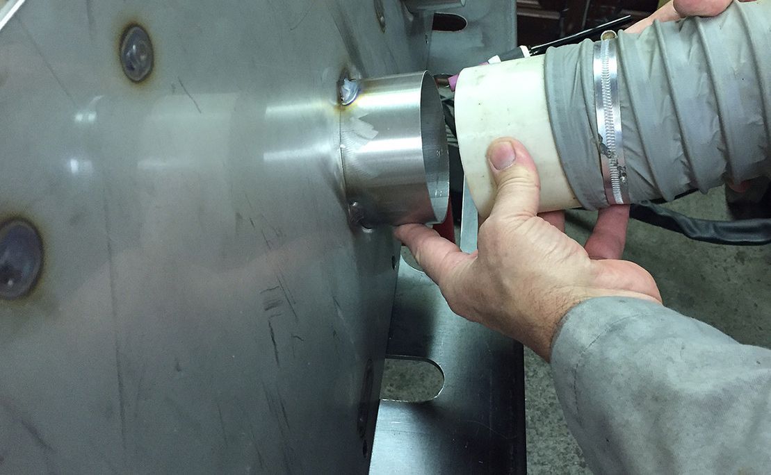 A person connects a flexible white hose to a metal port on a flat, industrial steel surface.