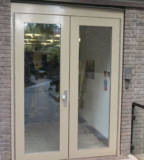 Beige double doors with glass panels set in a brick wall.