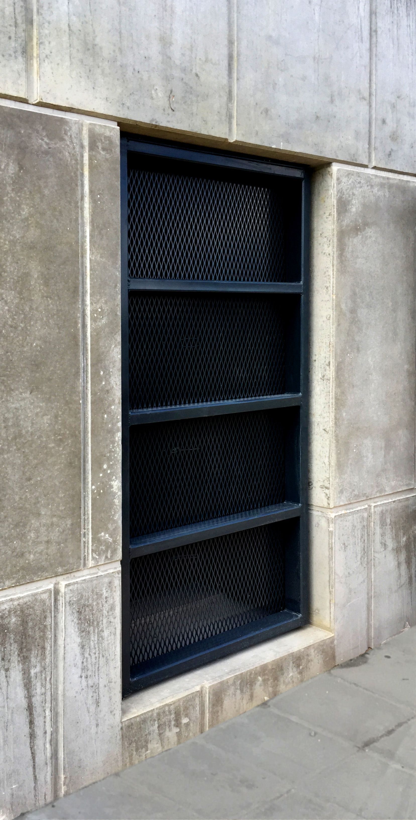 A black rectangular metal vent or screen set into a light-colored stone wall.