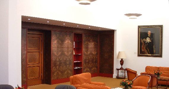 A formal room with orange armchairs, wood-paneled walls, a built-in bookshelf, and a framed portrait on a white wall.
